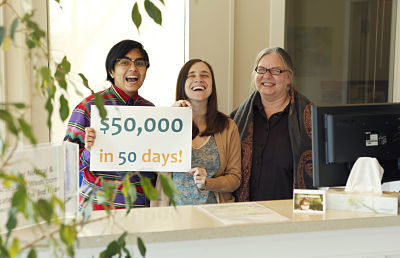 Three co-workers hold up a sign that says "$50,000 in 50 Days!"